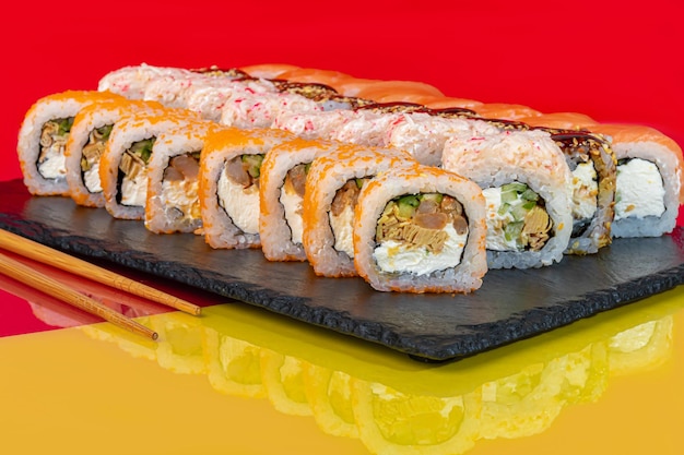 Nigiri sushi pone Uramaki California Filadelfia en un plato blanco Cerca de jengibre y salsa de soja wasabi en un tazón blanco Sobre un fondo de color