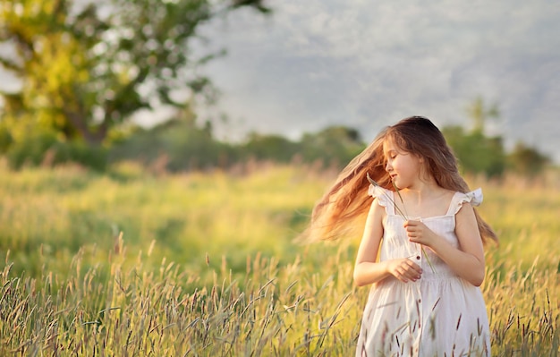 una niña de 10 a 11 años está parada en un campo y su cabello está soplando en el viento