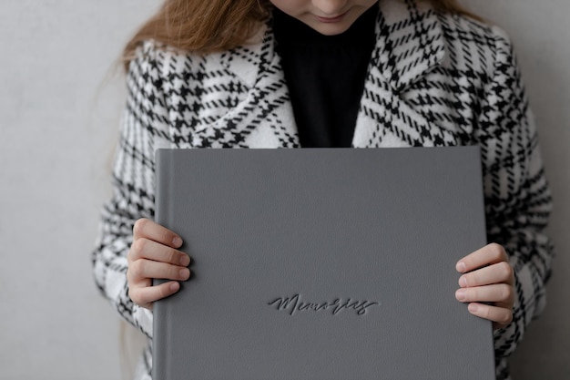 Una niña de 10 años está sentada sosteniendo un libro de fotografías de cuero gris.