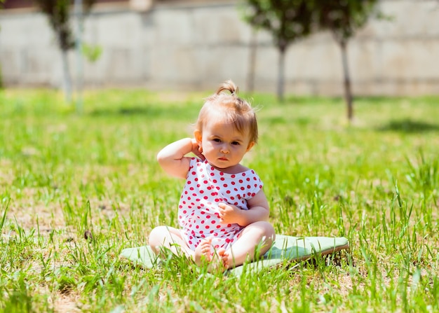 Niña de 11 meses está sentada en el parque sobre la hierba. niña con una chaqueta en guisantes se sienta en la hierba y juega con pompas de jabón.