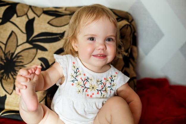 Una niña de 2 años está sentada en la cama y sonriendo. El niño se regocija y se da vuelta. Niño feliz