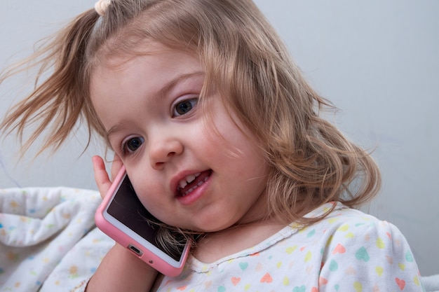 Niña de 2 años con un teléfono en la mano - jugando en casa mientras habla  por teléfono