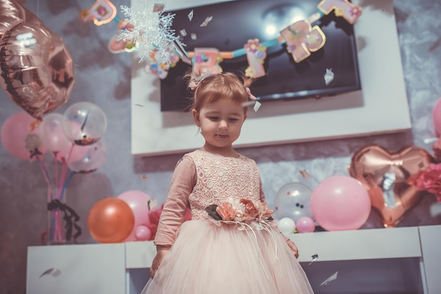 Niña de 2 años vestida de rosa con su primer pastel de cumpleaños, tarjeta de feliz cumpleaños, una linda niña celebra su primer cumpleaños rodeada de regalos