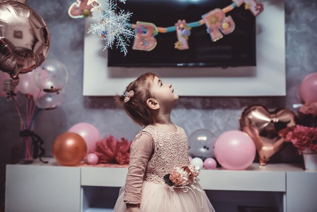 Niña de 2 años vestida de rosa con su primer pastel de cumpleaños, tarjeta de feliz cumpleaños, una linda niña celebra su primer cumpleaños rodeada de regalos