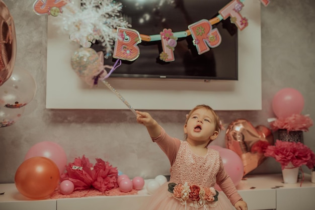 Niña de 2 años vestida de rosa con su primer pastel de cumpleaños, tarjeta de feliz cumpleaños, una linda niña celebra su primer cumpleaños rodeada de regalos