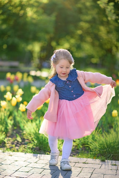 Una niña de 3 años camina por el parque con un vestido y un suéter rosa.