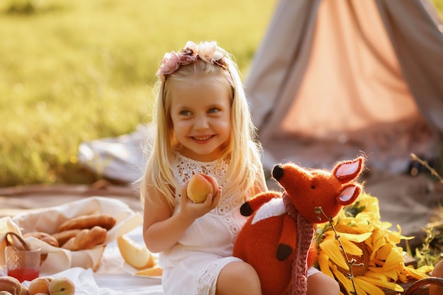 Niña de 3 años come melocotón en verano en un picnic