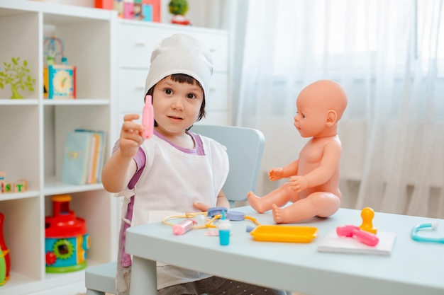 Niña de 3 años de edad preescolar jugando al doctor con muñeca el niño hace  un juguete de inyección