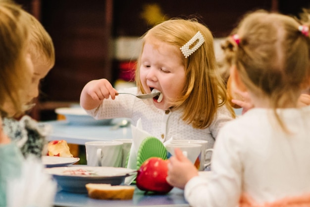 Niña de 3 años se sienta a la mesa y come independientemente Los niños comen en el jardín de infantes Almuerzo