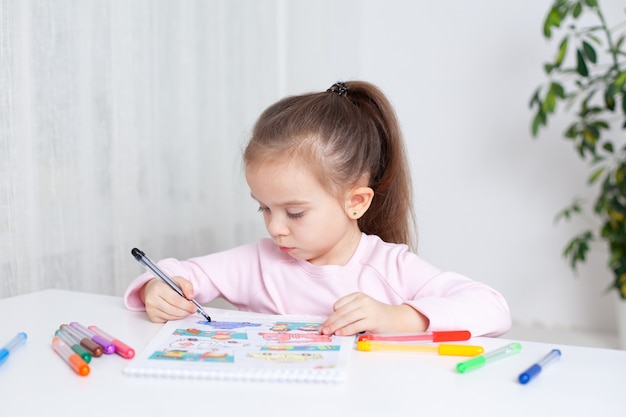 Una niña de 45 años dibuja diligentemente en los marcadores de color del álbum.