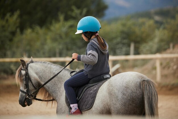 Foto niña de 5 años montando en un caballo en un club de hipico infalltil concepto de deporte