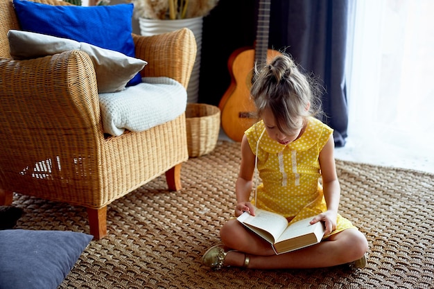 Niña de 6 años Su cabello estaba recogido en un moño Ella lee el libro con placer Vestido amarillo hermoso interior Deseo de aprender amor por la lectura