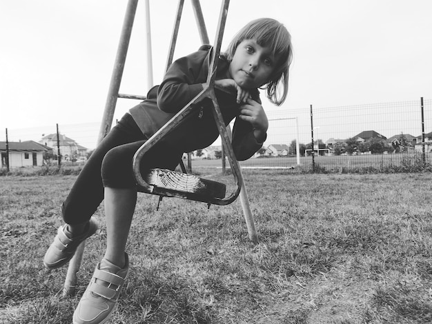 Una niña de 67 años columpiándose en un columpio contra el fondo de un campo de fútbol Imagen monocromática en blanco y negro en estilo retro o vintage Niño caucásico