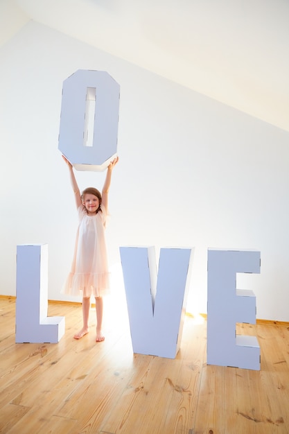 Niña de 7 años jugando con cartulina grande Letras 3D de pie formando la palabra AMOR