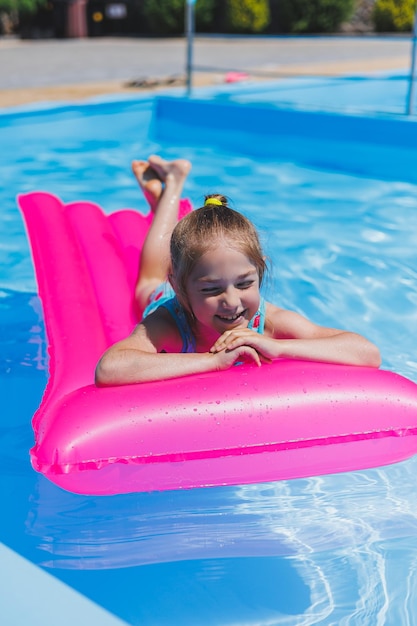 Niña de 78 años nada en la piscina sobre un colchón rosa inflable Vacaciones de verano