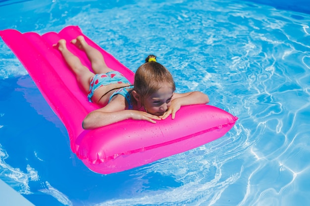 Niña de 78 años nada en la piscina sobre un colchón rosa inflable Vacaciones de verano