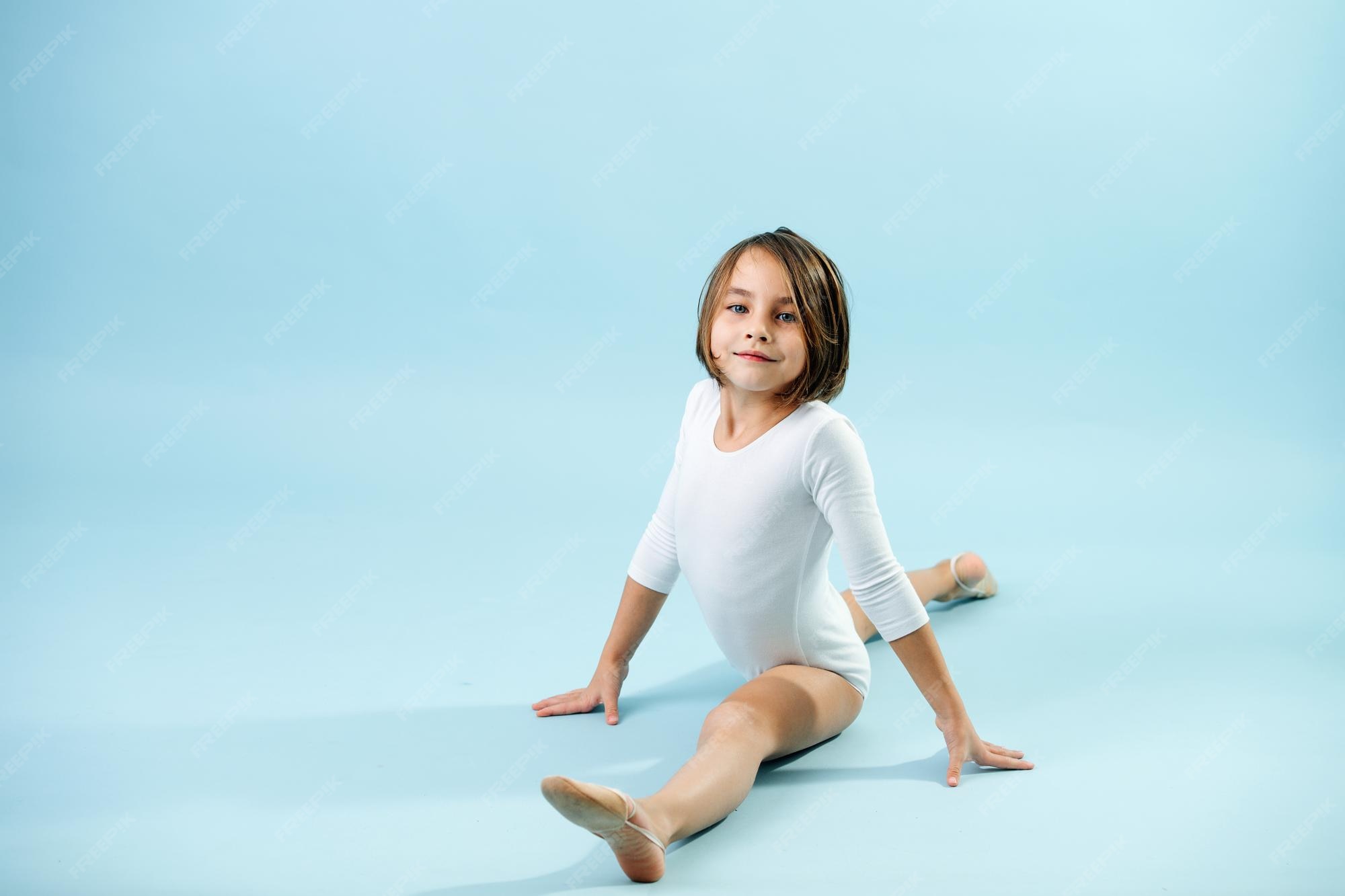 Niña de 8 años con un leotardo blanco haciendo divisiones mirando a la
