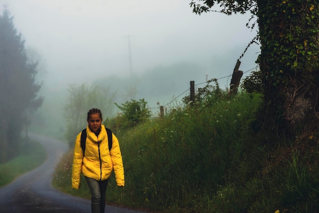 Una niña de 9 años con mochila va a la escuela a lo largo de un camino rural por la mañana sola en primavera