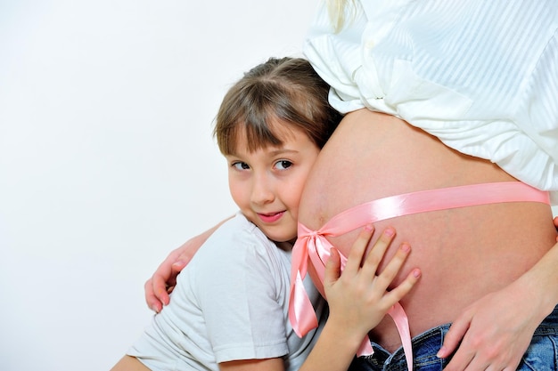 La niña abraza el estómago de la madre embarazada atada con una cinta rosa