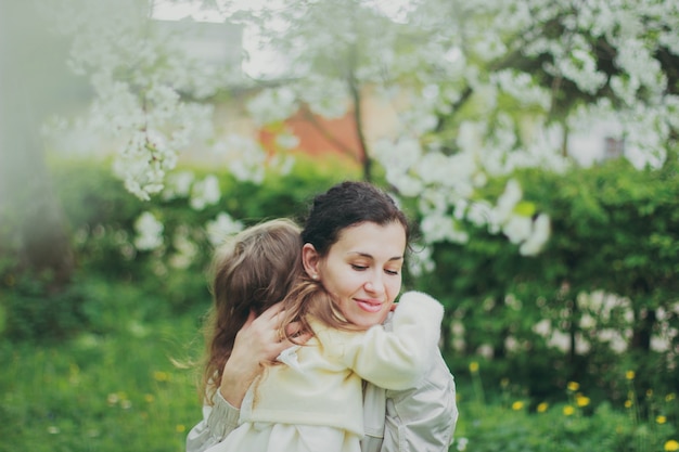 Niña abraza a su madre en el jardín de cerezos de primavera