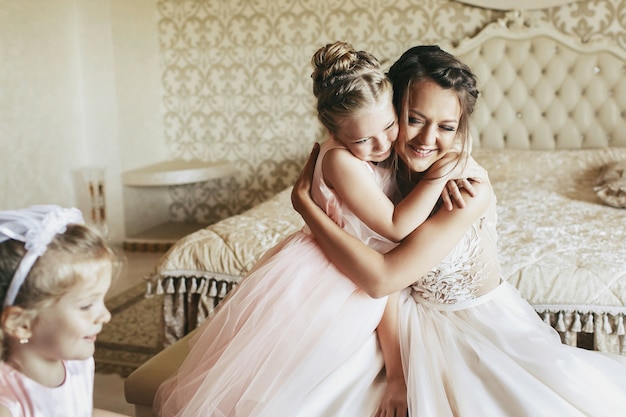 La niña abraza tierna novia hermosa en vestido de marfil