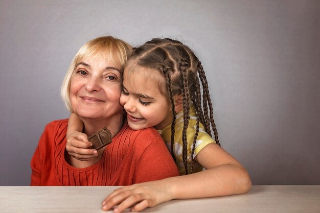 Niña abrazando a su abuela con amor y comiendo barras de chocolate con placer