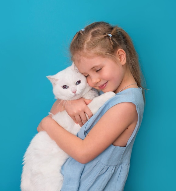 Niña abrazando a su mascota gato blanco sobre fondo azul.