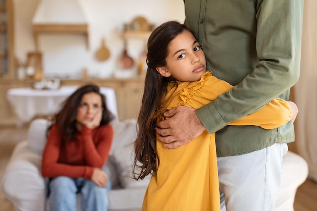 Niña abrazando a su padre con su madre en el fondo