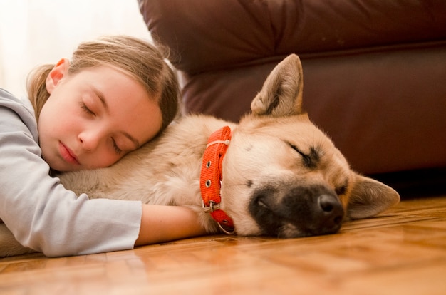 Niña abrazando a su perro y duerme en el piso