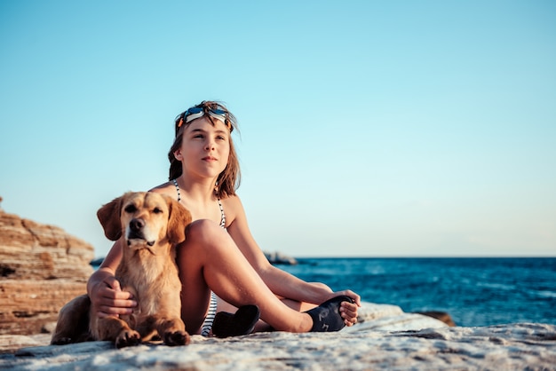 Niña abrazando a su perro mientras está sentado en la playa rocosa