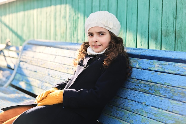 Niña con un abrigo azul en un banco del parque en otoño. Foto de alta calidad