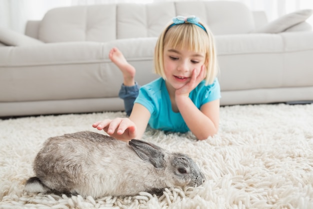 Niña acostada en la alfombra acariciando el conejo