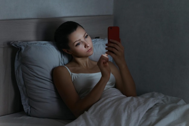 Niña acostada en la cama a altas horas de la noche y usando su celular para enviar mensajes en las redes sociales