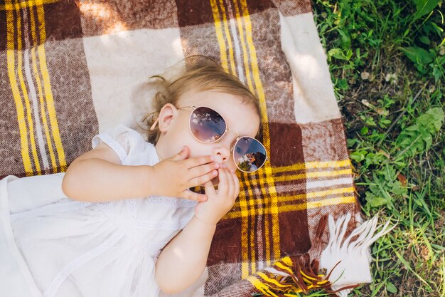 Foto una niña está acostada sobre una colcha a cuadros y probándose gafas de sol.