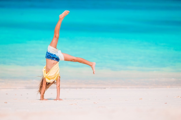 Niña activa en la playa divirtiéndose mucho. Chico lindo haciendo ejercicios deportivos en la orilla del mar