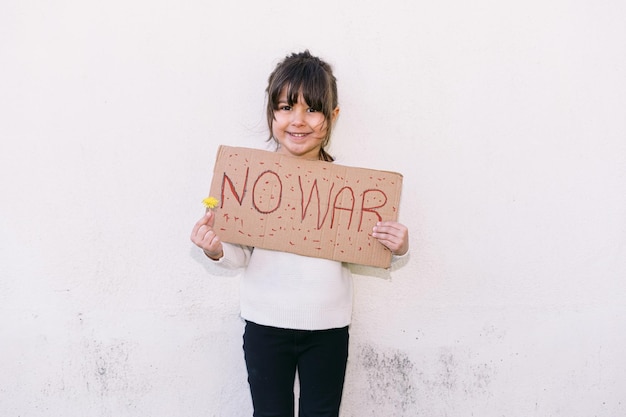 Niña activista sonriendo contra la guerra sostiene un cartel que dice 39NO WAR39 y una flor amarilla Concepto de guerra confrontación activismo paz y amor