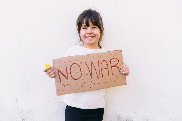 Niña activista sonriendo contra la guerra sostiene un cartel que dice 39NO WAR39 y una flor amarilla Concepto de guerra confrontación activismo paz y amor