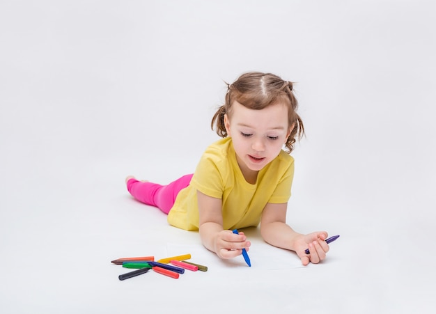 La niña se acuesta boca abajo y dibuja con lápices sobre papel. Aprendiendo a dibujar
