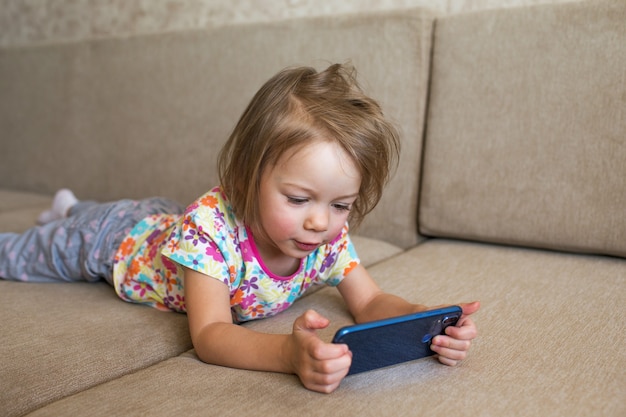 Una niña se acuesta en el sofá y mira el teléfono.