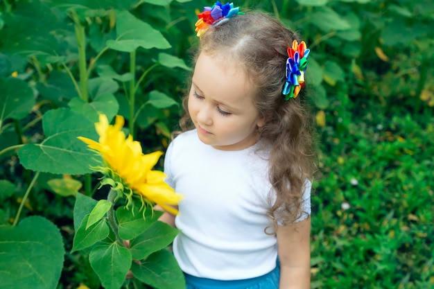 una niña admira una flor en un campo de girasoles