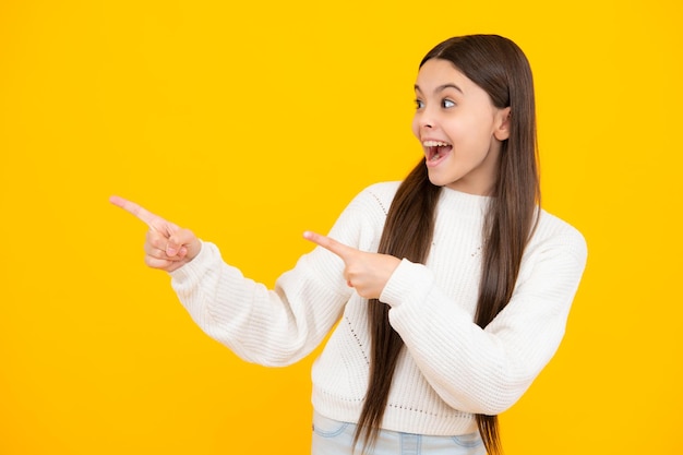 Niña adolescente apuntando hacia un lado con un dedo para presentar un producto o una idea Chica adolescente con ropa informal señalando un espacio vacío Cara emocionada Expresión asombrada alegre y contenta