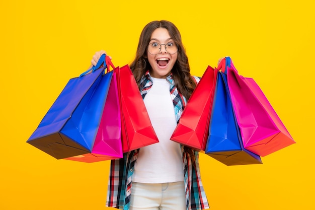 Niña adolescente asombrada Niña sostiene una bolsa de compras disfrutando de la venta aislada en un fondo amarillo Retrato de una adolescente está lista para ir de compras Expresión emocionada alegre y contenta