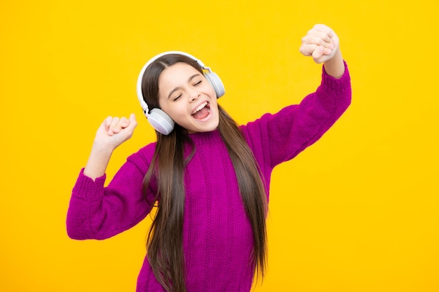 Niña adolescente con auriculares escuchando música con un elegante atuendo informal aislado sobre un fondo amarillo