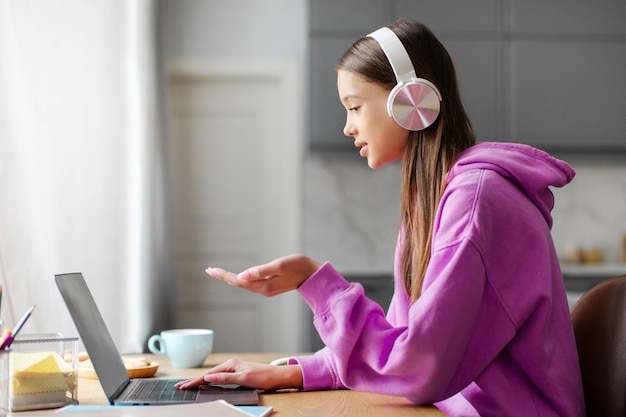 Niña adolescente con auriculares y usando portátil estudiando en línea desde casa participando en una sesión remota