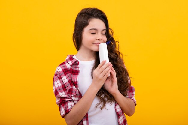 Niña adolescente con botella de champú o gel de ducha aislado sobre fondo amarillo Producto cosmético para el cabello para niños