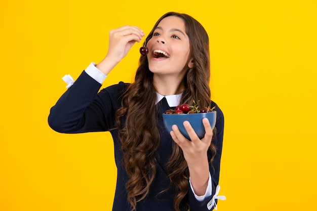 Niña adolescente comiendo cerezas aisladas sobre fondo amarillo Bayas de verano niños cerezas saludables