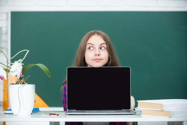 Niña adolescente estudiante con portátil en la escuela Estudiante adolescente trabajando en portátil en el aula Niña pequeña usando portátil muestra y apunta a la pantalla del monitor Concepto de educación en el hogar Lección escolar