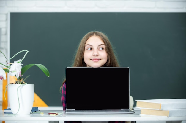 Niña adolescente estudiante con portátil en la escuela Estudiante adolescente trabajando en portátil en el aula Niña pequeña usando portátil muestra y apunta a la pantalla del monitor Concepto de educación en el hogar Lección escolar
