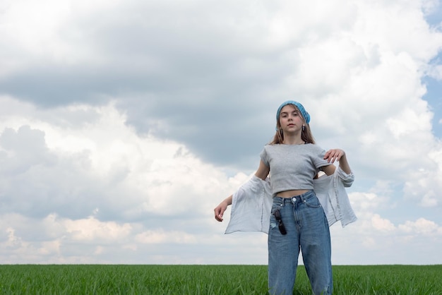 Niña adolescente de moda en un campo de hierba verde contra un fondo de cielo nublado