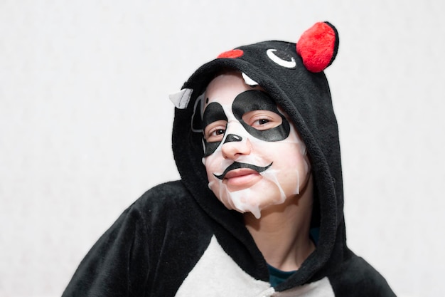 Foto una niña, una adolescente con un murciélago kigurumi y una máscara cosmética en la cara en forma de panda.